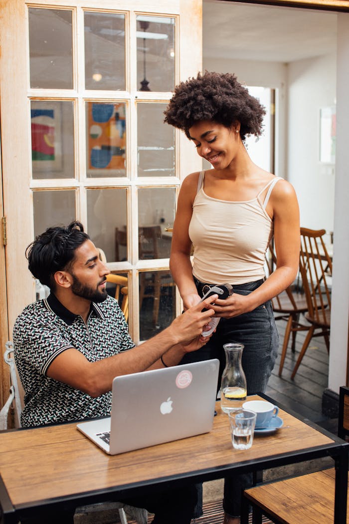 A man and woman smiling during a transaction using a pay terminal in a cozy cafe.